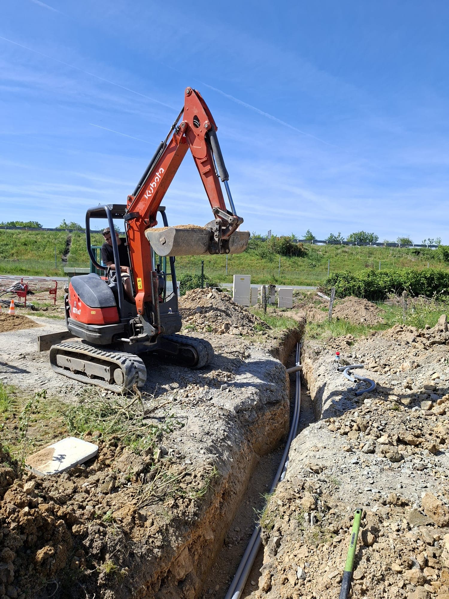 Mini-pelle Kubota en plein creusement de tranchee sous un ciel bleu